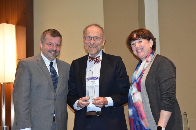 Two men and woman smiling with the man in the center holding a glass award