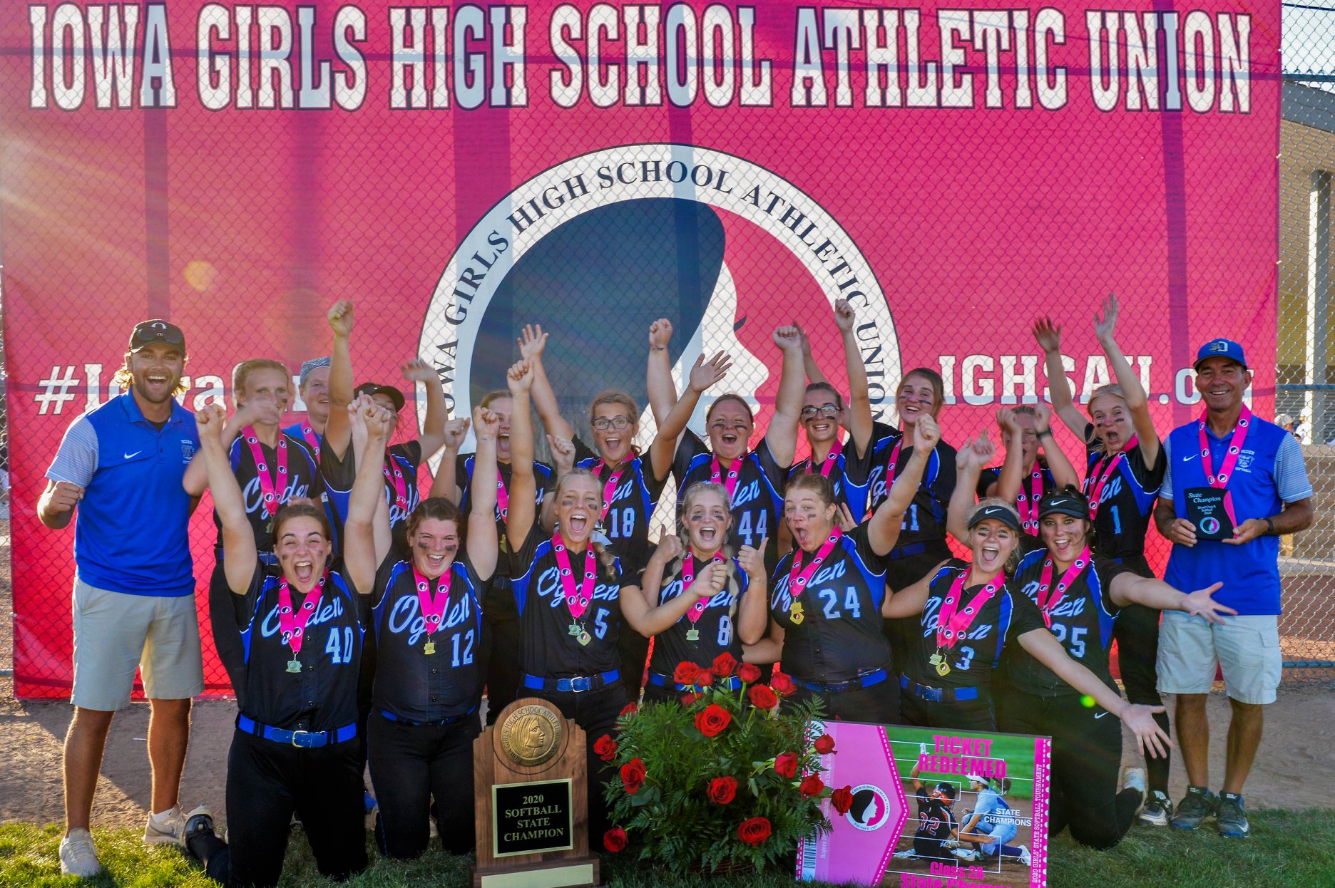 Softball team holding medals and smiling in from of Iowa Girls High School Athletic Union sign