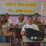 Eight students sitting at desks in front of sign that says "life is short... so run long"