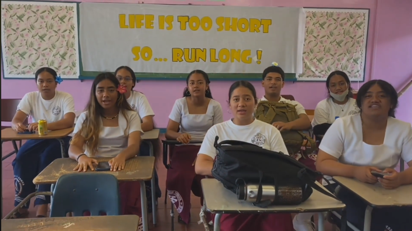 Eight students sitting at desks in front of sign that says "life is short... so run long"