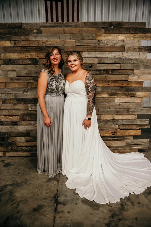 Two women smiling together, one in a wedding dress the other in a gray gown.