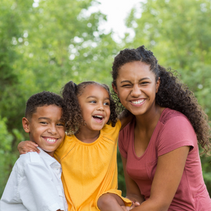 Pictured left to right is a young boy, young girl, and young woman holding each other and smiling