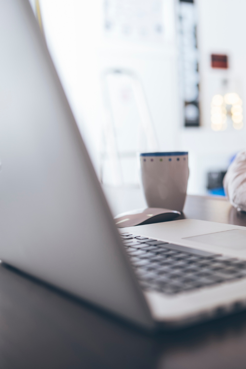 Photo of a laptop on top of a desk. A cup can be seen next to the laptop.