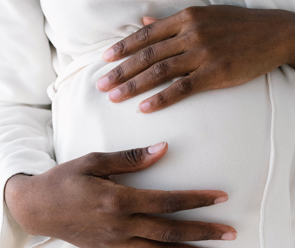 Close-up of a pregnant person's belly. Their two hands are placed on top of their belly.