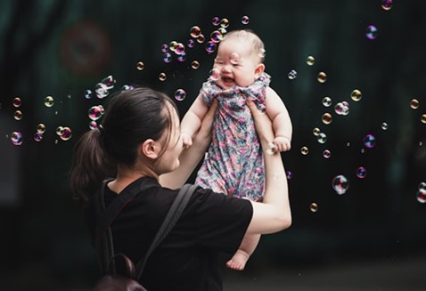 A mother lifting her smiling infant in the air with bubbles swirling around them