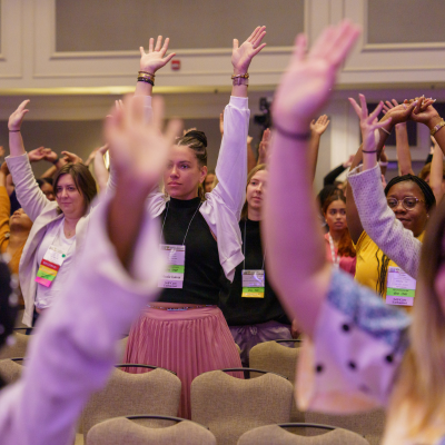 Photo of diverse leaders at one of AMCHP's conferences raising their hands during one of the plenary sessions.